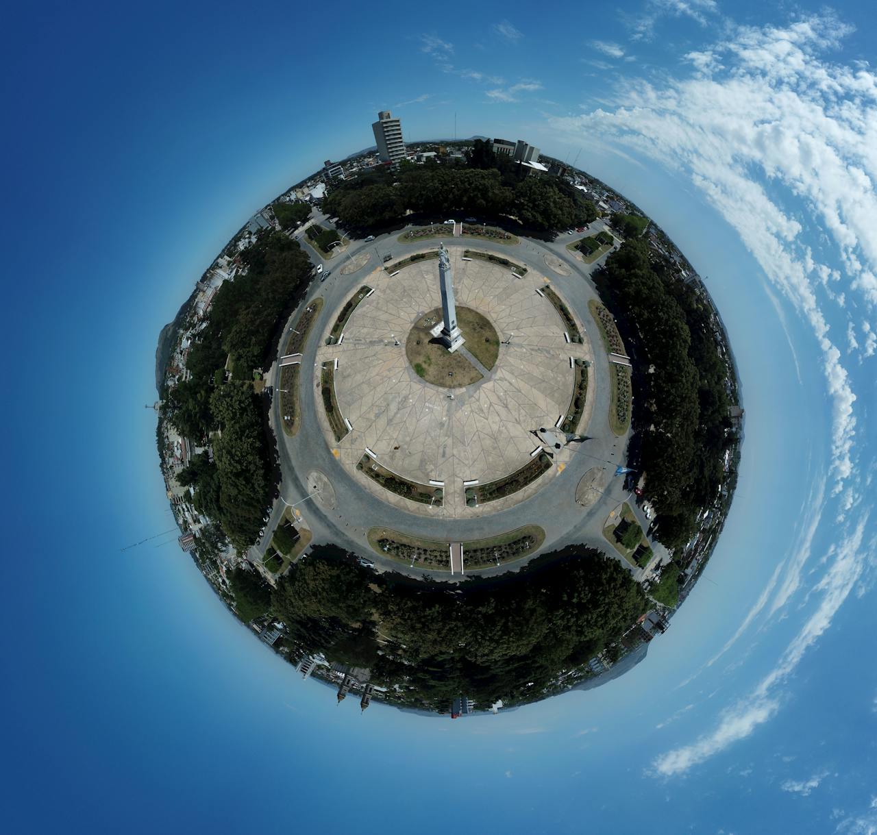 Home Aerial fisheye landscape view of a circular monument in Balcarce, Argentina under a blue sky.